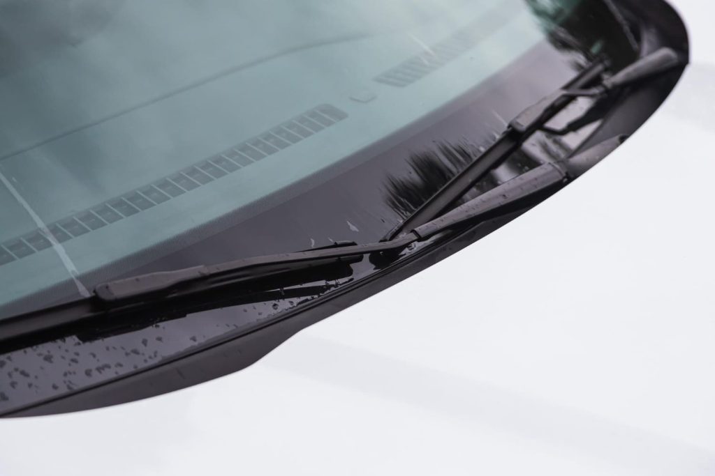 Parabrisas de coche con gotas de agua y limpiaparabrisas en reposo, destacando la homologación de las lunas y su mantenimiento - Carglass.