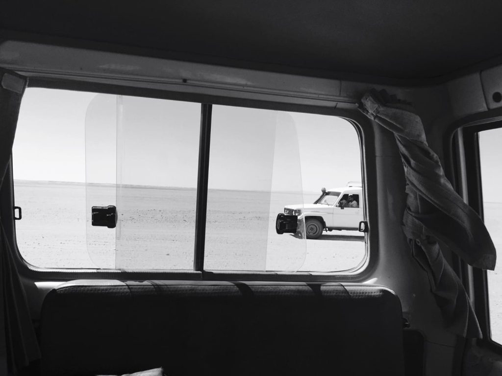 Vista desde el interior de un coche hacia una ventana lateral con otro vehículo estacionado en el desierto - Carglass.