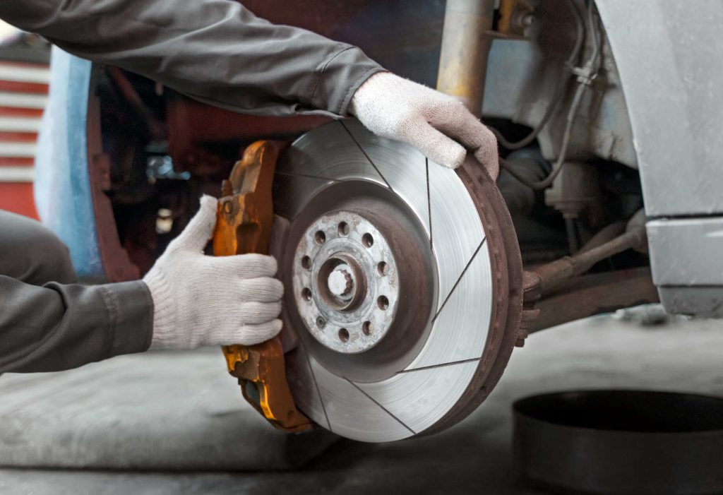 Un mecánico inspecciona y ajusta el disco de freno de un automóvil utilizando guantes protectores. Imagen representativa del mantenimiento de frenos y sistemas de seguridad vehicular