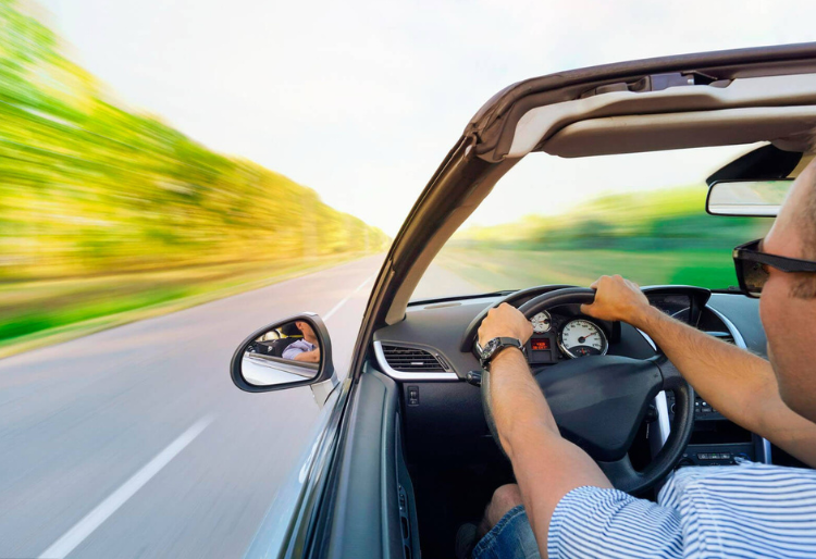 Persona conduciendo un coche a alta velocidad en una carretera despejada, vista desde el interior con enfoque en el volante y el tablero de instrumentos. - Carglass.