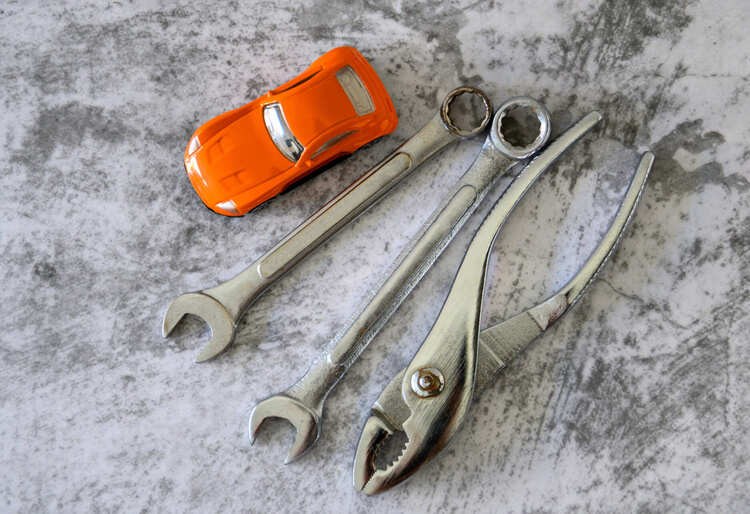 Kit de emergencia para coche con pinza, llaves de boca y coche de juguete naranja sobre superficie gris, ideal para mantenimiento - Carglass