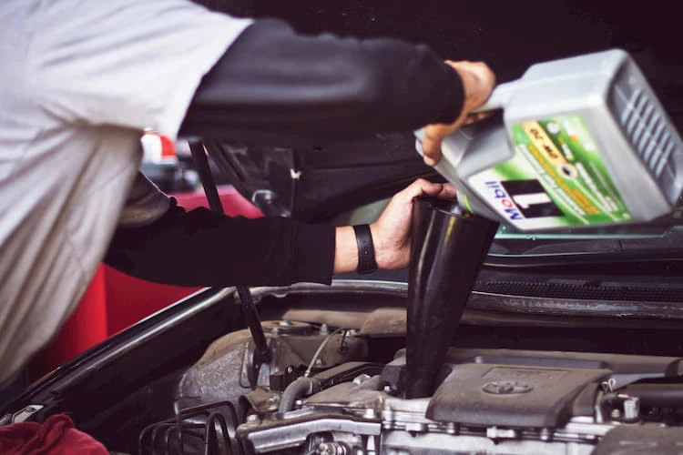 Persona rellenando líquido en el motor de un coche con un embudo, destacando la importancia del líquido refrigerante coche - Carglass.