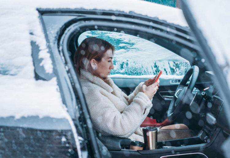 Mujer dentro de un coche encendido con cristales cubiertos de nieve, ilustrando cómo arrancar coche en frío durante el invierno - Carglass.