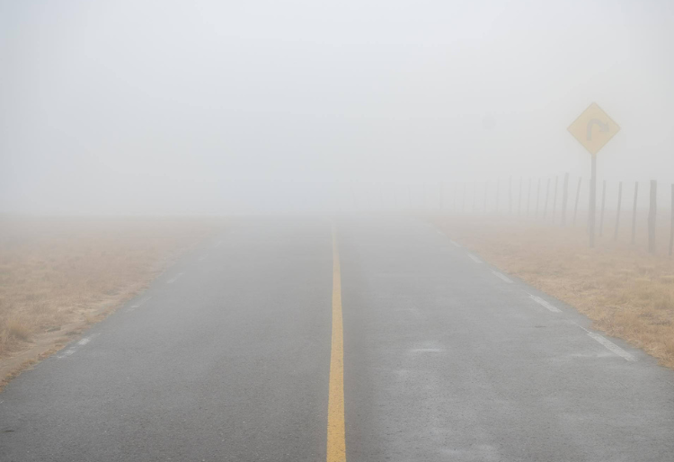 Carretera cubierta de niebla con señal de curva a la derecha visible al fondo - Carglass