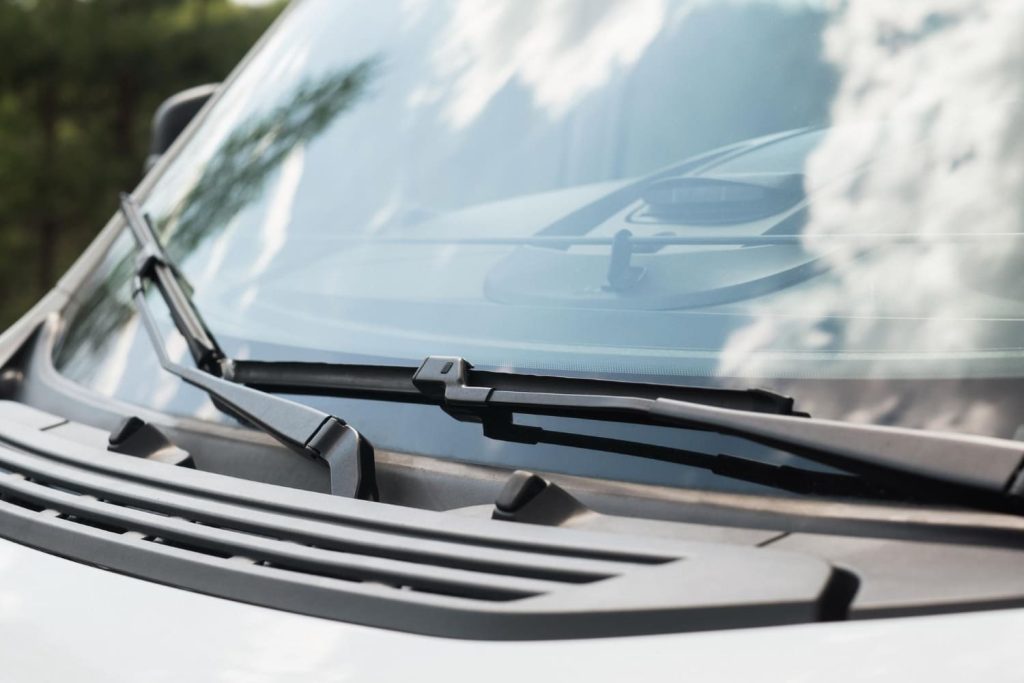 Parabrisas de coche con reflejos de nubes y limpiaparabrisas en primer plano, resaltando claridad y resistencia del cristal laminado en lunas de coche - Carglass.