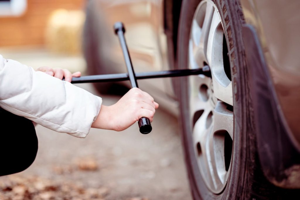 Persona cambiando una rueda de repuesto con una llave cruz. Pensando sobre los kilómetros de uso de una rueda de repuesto - Carglass.