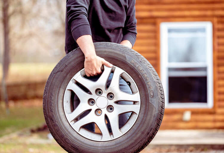 Persona con sudadera negra sostiene una rueda de repuesto, clave para conocer los kilómetros de una rueda de repuesto antes de cambiarla - Carglass.