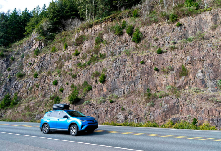 " Coche azul en ruta peligrosa junto a acantilado rocoso con vegetación en la Ruta da Morte - Carglass."