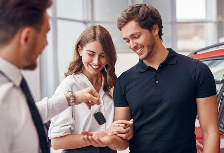 Pareja sonriente recibiendo las llaves de su nuevo vehículo en un concesionario, ideal para ilustrar el tema cómo hacer el rodaje de un coche - Carglass.