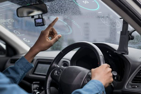 Innovaciones en diseño de lunas y parabrisas inteligentes con el sistema ADAS: persona conduciendo al volante y señalando la luna con imágenes proyectadas