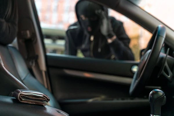 Grabación de matrícula coche: primer plano de un coche en el que hay un ladrón asomado a la ventanilla y mirando a una cartera con billetes que hay en el interior