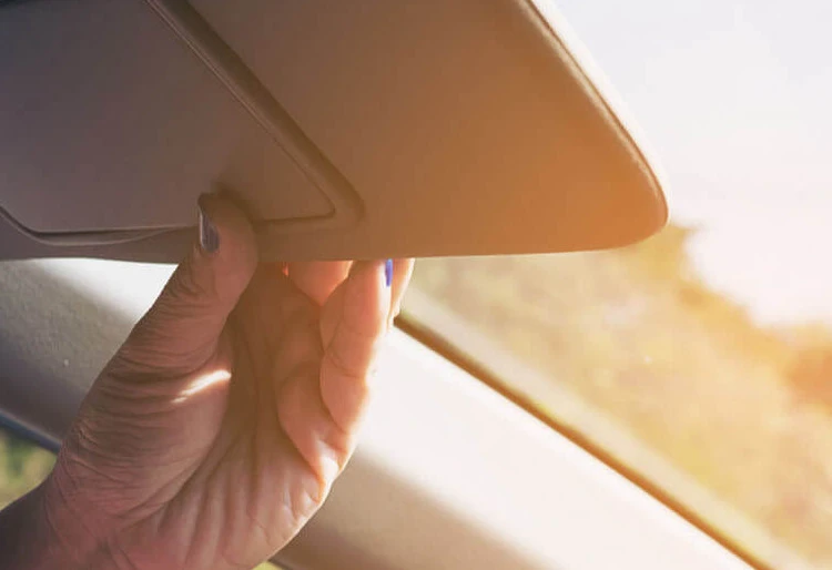 Protección UV - Carglass: persona colocando el espejo del coche para que no la refleje el sol