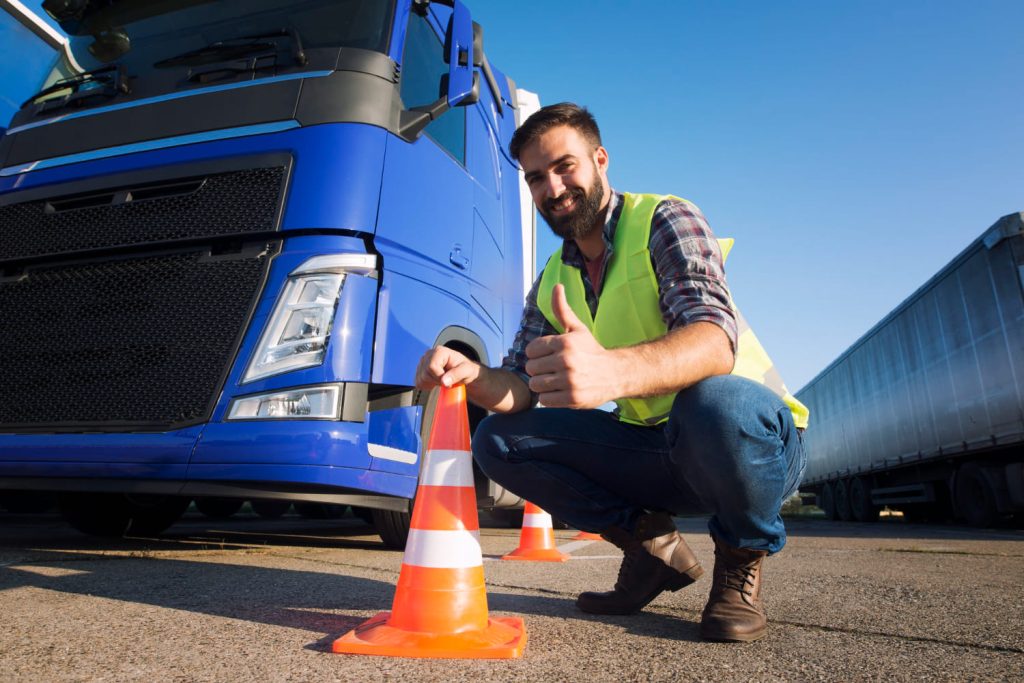 Hombre con chaleco reflectante y conos de seguridad frente a un camión azul en revisión de seguridad - dispositivos de seguridad para camiones - Carglass.