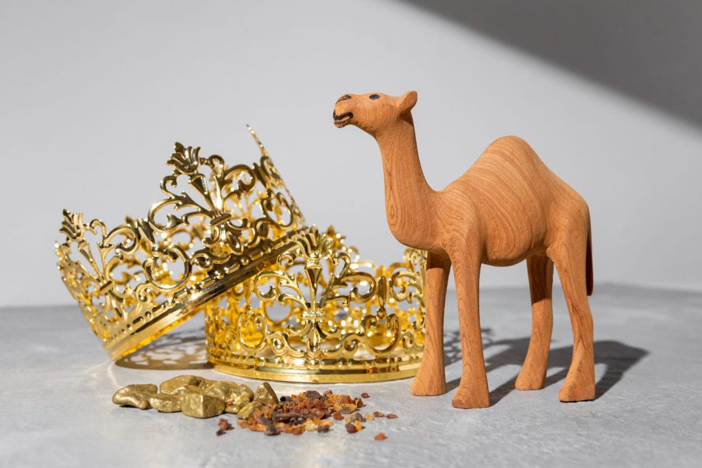 Figura de un camello de madera junto a dos coronas doradas y regalos de los Reyes Magos, evocando cabalgatas en pueblos de España - Carglass.