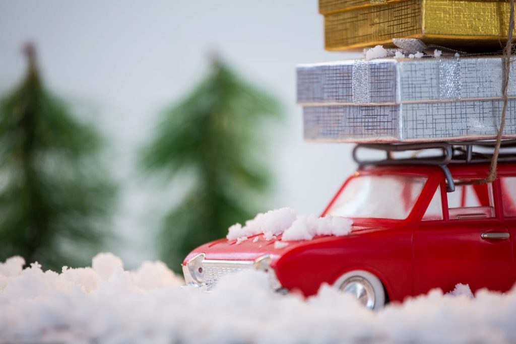 Un coche rojo con nieve lleva regalos en su techo, destacando un ambiente navideño perfecto para consejos de conducción - Carglass.