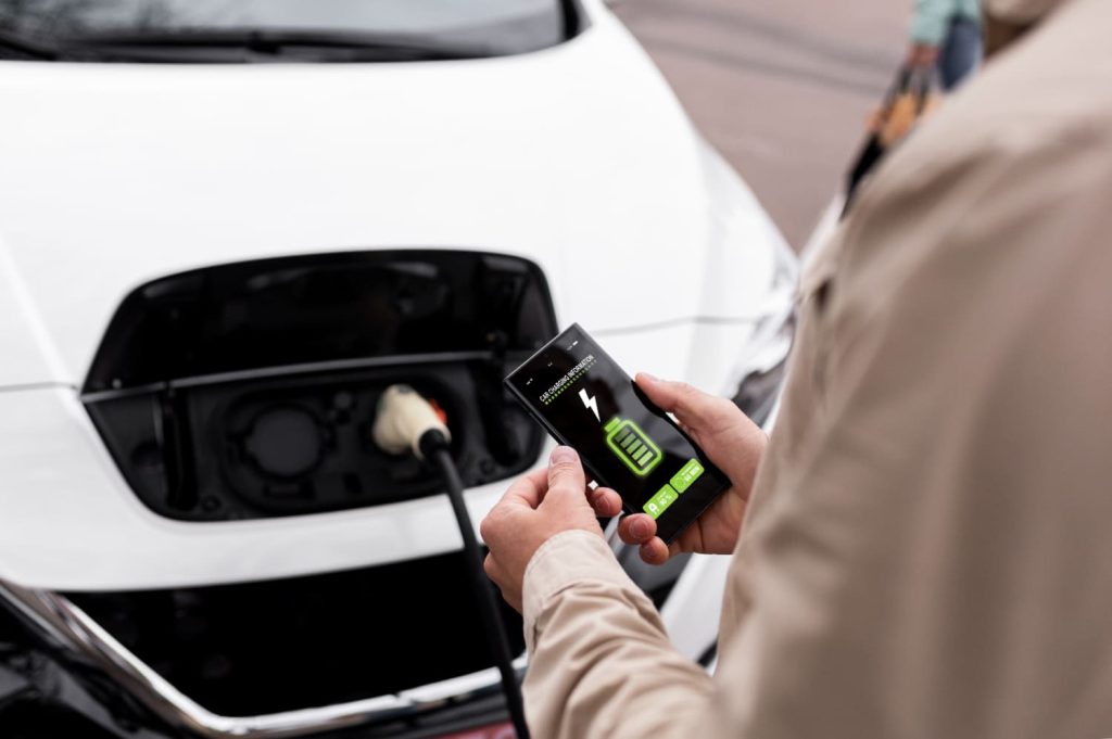 Una persona sostiene un móvil que muestra el estado de carga de un coche eléctrico conectado a una estación de carga, resaltando la opción de alquilar coche eléctrico - Carglass.