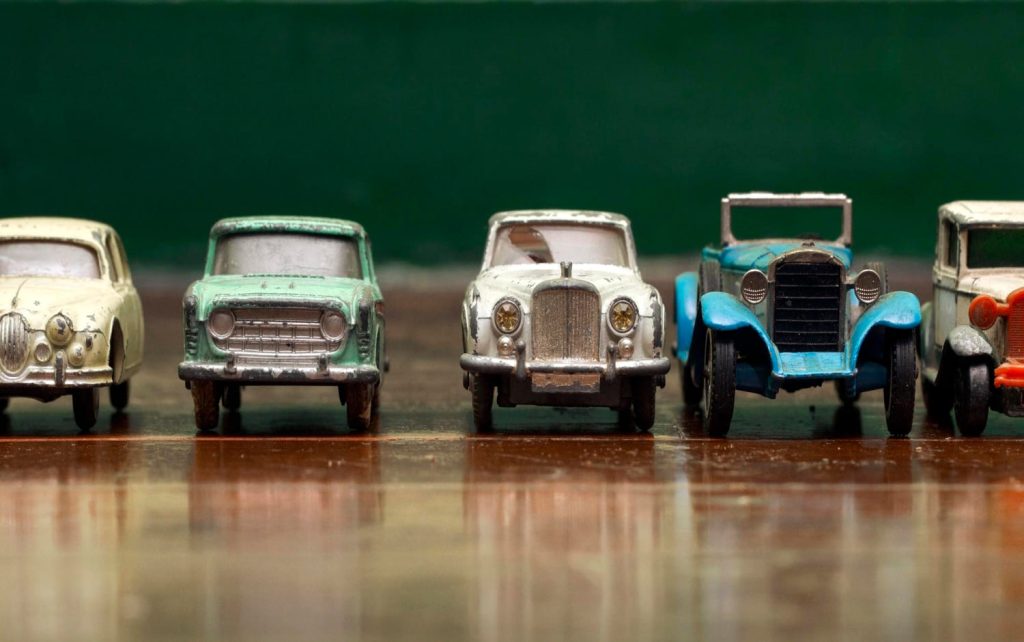 Conjunto de coches clásicos en miniatura, alineados sobre una superficie de madera con fondo verde. Ideal para coleccionistas apasionados del modelismo - Carglass.