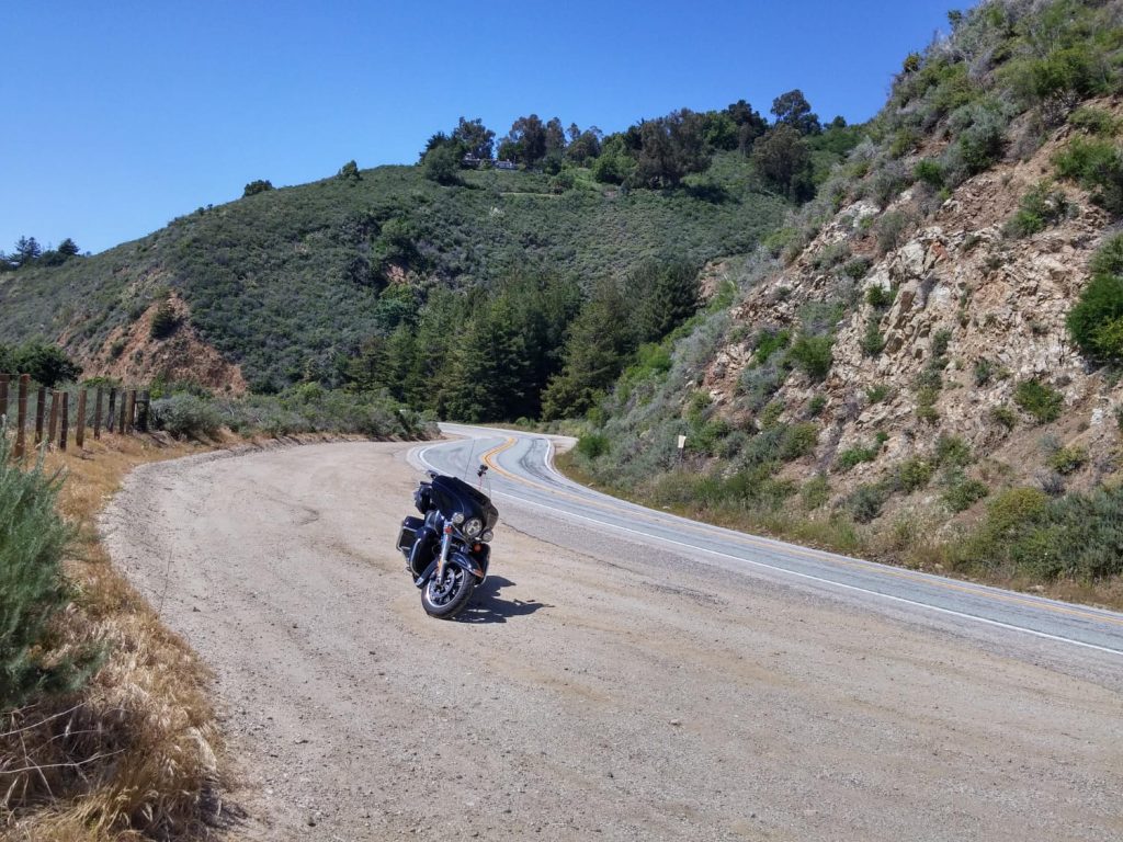 
Moto aparcada en una curva de una carretera rodeada de colinas verdes bajo un cielo despejado - Carglass.