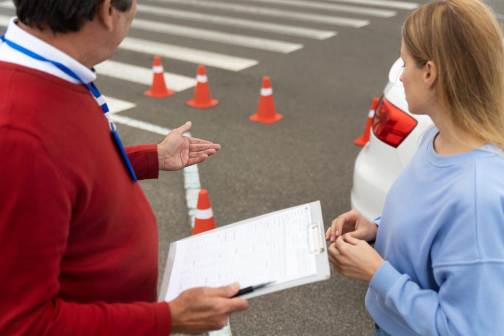 nstructor con carpeta explicando a una mujer junto a conos de tráfico y un coche, representando cambios en la normativa DGT 2025 - Carglass.