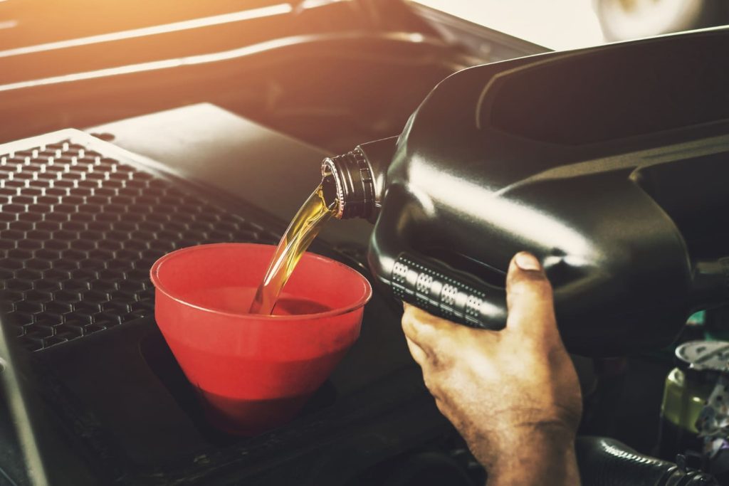 Mano de una persona vertiendo aceite de motor desde un recipiente negro. Realizando el mantenimiento del motor del coche - Carglass.