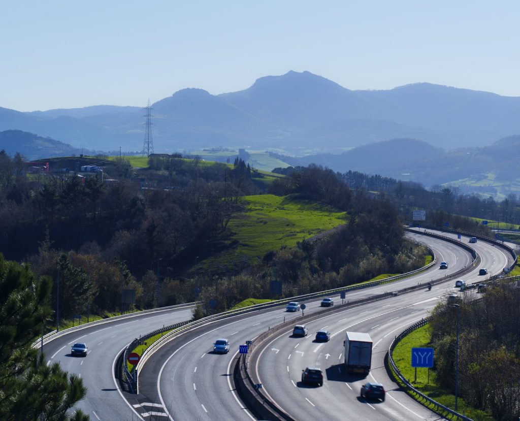 Autovía en España con curvas cerradas y tráfico en ambos sentidos, rodeada de montañas y naturaleza. Carreteras peligrosas en España - Carglass.