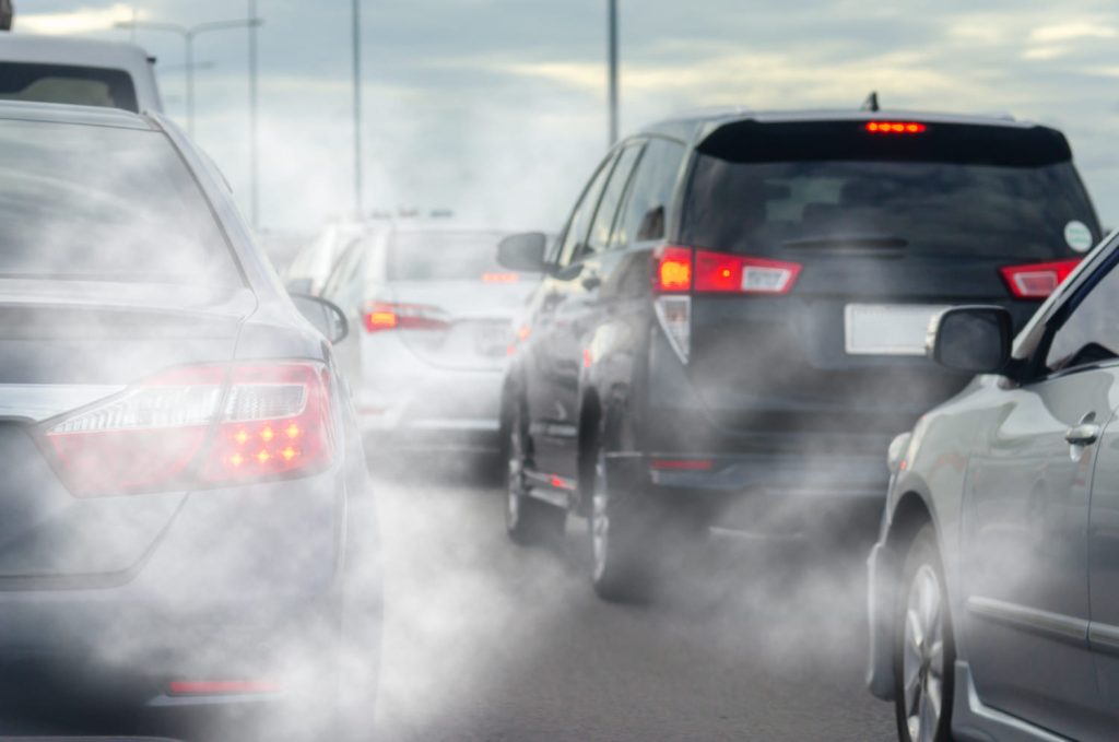 Tráfico denso con coches emitiendo humo del escape, ideal para contenido sobre consejos para que tu coche contamine menos - Carglass.