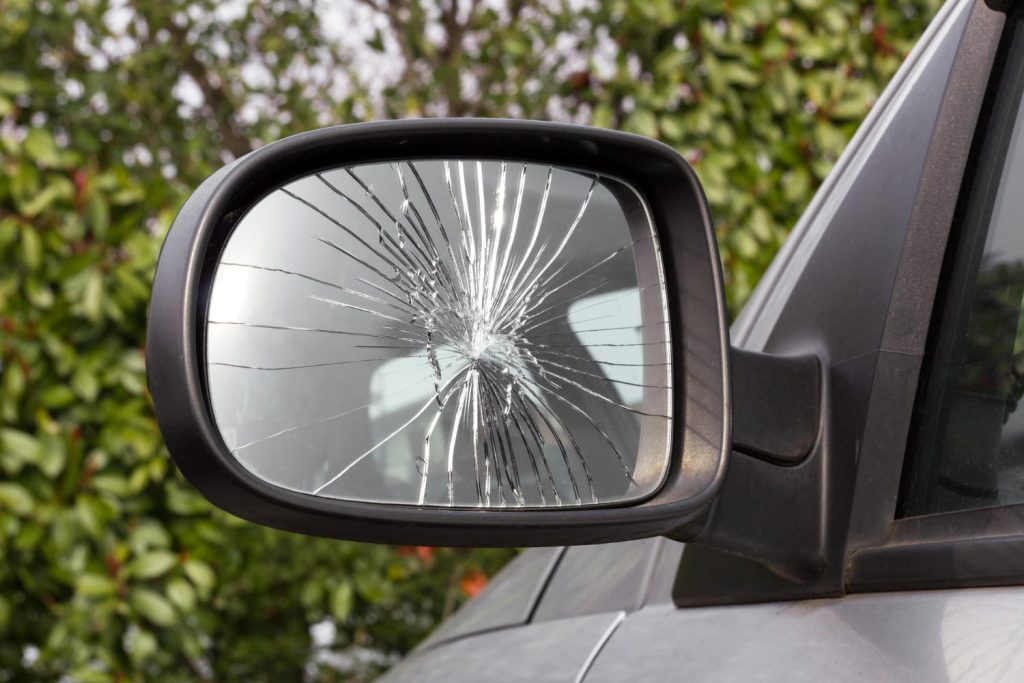 Retrovisor lateral de auto con el vidrio roto por impacto, usado para ilustrar consejos sobre cómo proteger retrovisores del daño - Carglass.