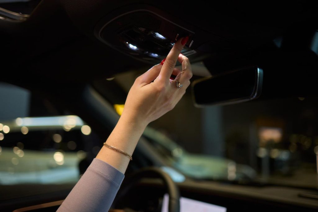 Mano encendiendo las luces de cortesía interior de un coche moderno, resaltando detalles de lujo y confort - Carglass.