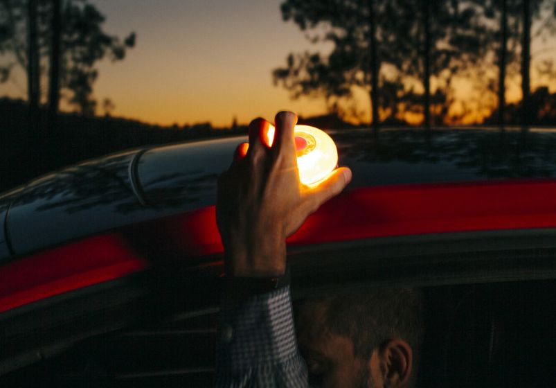 Help flash: persona colocando la luz de emergencia help flash encima de un coche rojo con un paisaje de fondo con árboles